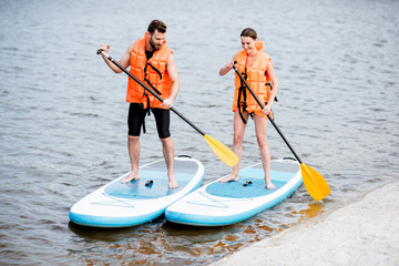 Couple in life vests learning to row on the stand up paddleboard on the lake