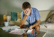 © TheVisualsYouNeed - young attractive worried and stressed man at home calculating month tax expenses with calculator accounting payments doing bank paperwork in stress