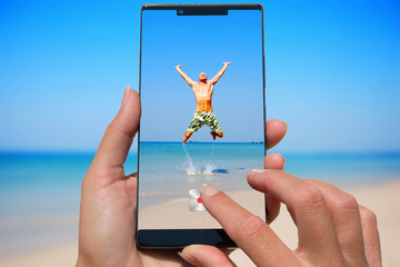 Woman with mobile phone photos man on the exotic beach.