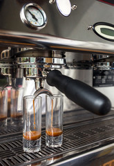 Close-up of espresso pouring from coffee machine into the two tall glasses. 