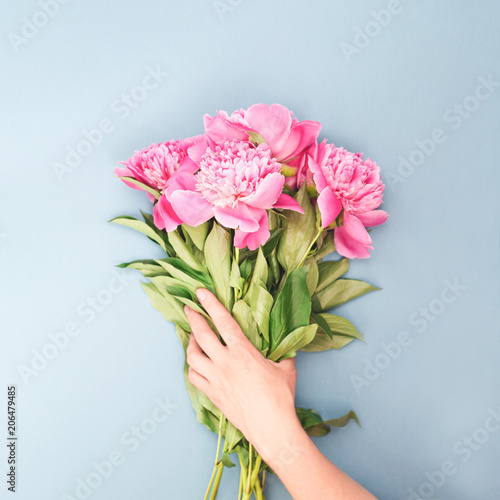 Female hand holding bouquet of pink peony flowers. Holiday background, top view.