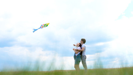 Young family, couple running a kite against a blue sky and clouds