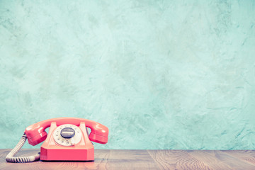 Fototapete - Retro classic outdated pink rotary telephone on wooden desk front textured aquamarine concrete wall background. Vintage instagram old style 