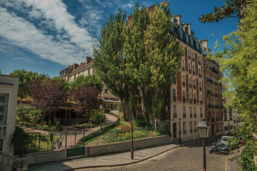 Sticker - Apartment buildings and wooded gardens under sunny blue sky in a street of Montmartre at Paris. Known as the “City of Light”, is one of the most impressive world’s cultural center. Northern France.