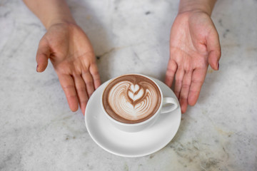 The latte art in the white mug on the white marble table with the man or woman hands. 