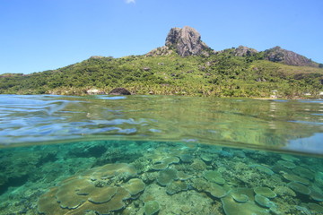 Over Under Shot of a tropical island in Fiji showing the coral reef underwater and a rocky mountain on the island