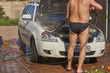 A man washes a motor off a white car with an open hood