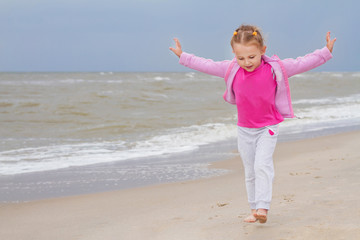happy little child girl with hands to the side and dressed in pink running by the sea beach