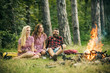 © Volodymyr - Happy friends enjoying evening outdoors. Young man and two women sitting around campfire. Friends camping in wilderness