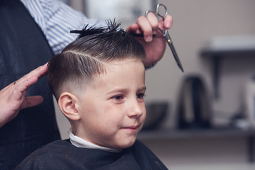 Cheerful Caucasian boy  getting hairstyle in barbershop.