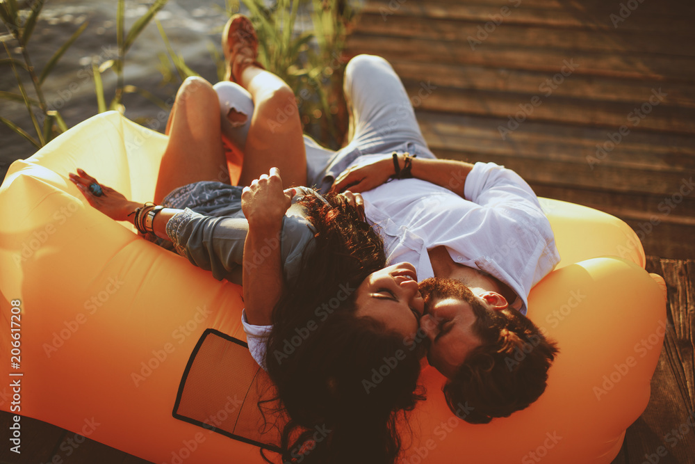 Young couple lying in a lazy bag during the sunset - obrazy, fototapety, plakaty 