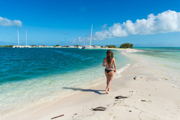 Wall Mural - Thin girl with a black bikini walking on a beautiful beach in the Caribbean Sea