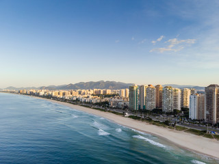 aerial landscape photo of Barra da Tijuca beach , with waves crashing on beach during sunrise, with the beachfront buildings in the background