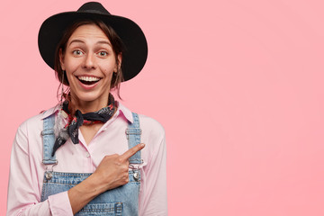 Wall Mural - Adorable young female gardener wears countryside clothes, advertises poison for insects, being delighted with its effect, stands against pink wall with blank space. People and farming concept