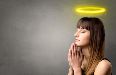 Young woman praying on a grey background with a shiny yellow halo above her head