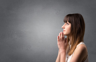 Young woman praying on a grey background