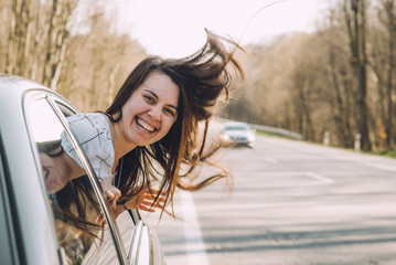 Wall Mural - young pretty woman stick out of car window. wind blowing woman hair