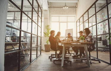 Full length concentrated female and men partners looking at mobile and working with notebook computers while locating at desk. Orderly team concept