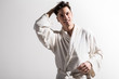 © Yakobchuk Olena - Ready to new day. Portrait of cheerful cute young man in white terrycloth bathrobe is looking forward with smile. He is standing against light wall with raised hand. Male beauty concept. Copy space
