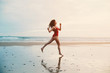 © Annatamila - Woman wearing red swimming suite running on ocean beach at sunset, Lisbon, Portugal