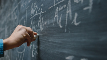 Wall Mural - Close-up Shot of a Hand Holding Chalk and Writing Complex and Sophisticated Mathematical Formula/ Equation on the Blackboard.
