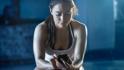 beautiful athletic brunette uses smartphone while resting on the bench after her intensive cross fit