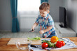 © olgasparrow - Cute little Blond boy was preparing to make a salad of green, yellow and red vegetables at the table