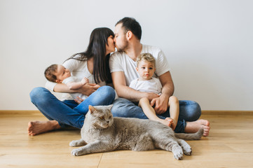 parents kissing each other with two sons and grey british shorthair cat on hands at home