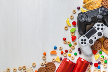 Wall Mural - black and white modern gamepads on a white wooden background among sweets, biscuits and cans of soda.