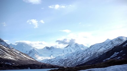 Canvas Print - Clouds are fast moving over high snow-capped mountains