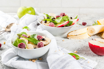 Wall Mural - Healthy summer breakfast, fruit and berry salad with spinach, granola, apple and banana, white marble background  copy space