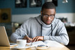 © fizkes - Focused millennial african american student in glasses making notes writing down information from book in cafe preparing for test or exam, young serious black man studying or working in coffee house