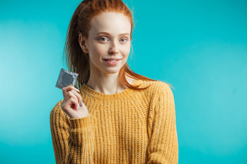 Attractive ginger adult woman holding condom calling to prevent sexually transmitted diseases or unwanted pregnancy