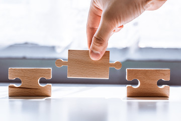 Hand holding a wooden jigsaw puzzle with blank space. There is a matching puzzle next to it. The concept of solving problems, all problems can be solved, connection.