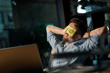 Cheerful adult man resting in office with sticky notes on the eyes. 