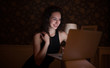 © maryadam - Happy pretty woman using laptop sitting on cosy sofa. Business woman works at home in night.