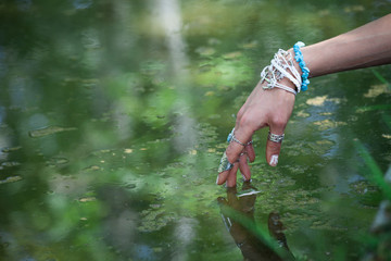 Wall Mural - woman hand touching water with boho style rings and bracelets enjoy in summer day on lake