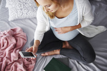 Pregnant Woman Using Mobile Phone At Bedroom