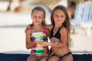 Two beautiful happy girl on the beach near the sea with shells in their hands