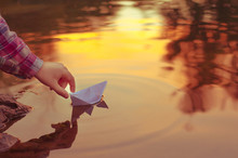The Child's Hand Launches A Paper Boat At Dawn Or Sunset