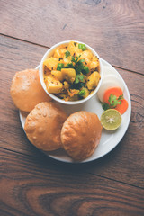 Wall Mural - Chatpate Masala Aloo Sabzi fry OR Bombay potatoes served with fried puri or Indian bread made up of wheat in a plate, selective focus