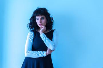 Portrait of a beautiful concerned young woman in an elegant dress standing in front of a white wall.