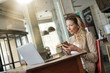© goodluz - Businesswoman using smartphone in front of laptop, sitting at coffeeshop