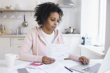 Concentrated young african american female student using online banking application with hand on touchpad, looking at screen of his laptop, trying to make payment for university education.