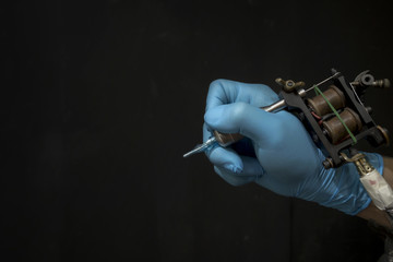 Tattoo artist holding a tattoo machine on dark background in studio.