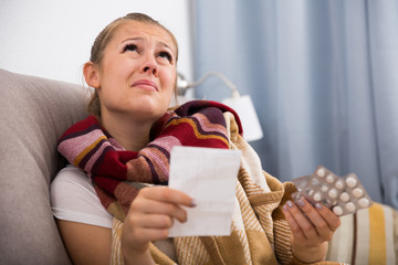 Sad young female reading recipe with pills