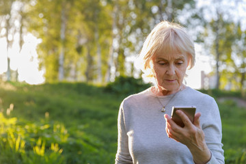 Elderly woman is holding a phone in her hand. Be careful on the Internet, fraud