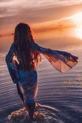 Wall Mural - beautiful young woman in elegan dress walking on water at sunset