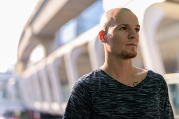 Young handsome bald man thinking against exterior of the mall in