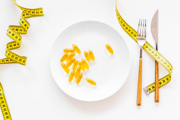 Wall Mural - Dietary supplement for well-being. Fish oil or omega-3 capsules on plate near measuring tape on white background top view